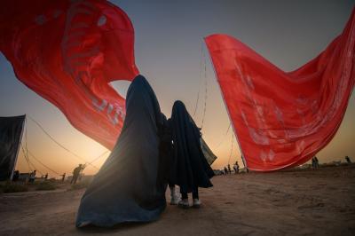 تحت راية العباس عليه السلام، وقفت السيدة زينب، لم تكن الراية قطعة قماش، بل كانت وصيّة أخٍ مضى دون أن يغيب، وعهداً مكتوباً بكفه المبتورة على صفحة الريح: أن تظلّ زينب مصونة، ولو بقي من العباس ظلّ راية فقط