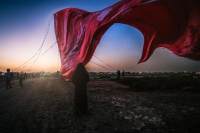 تحت راية العباس عليه السلام، وقفت السيدة زينب، لم تكن الراية قطعة قماش، بل كانت وصيّة أخٍ مضى دون أن يغيب، وعهداً مكتوباً بكفه المبتورة على صفحة الريح: أن تظلّ زينب مصونة، ولو بقي من العباس ظلّ راية فقط